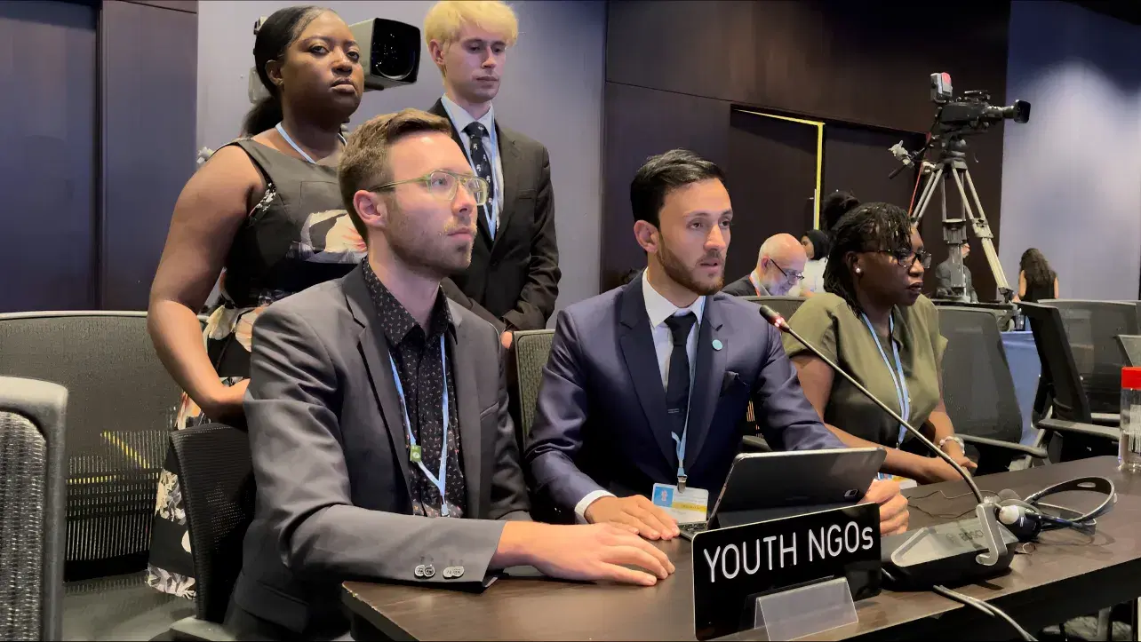 Youth delegates seated behind a YOUTH NGOs nameplate at an international climate negotiation session.