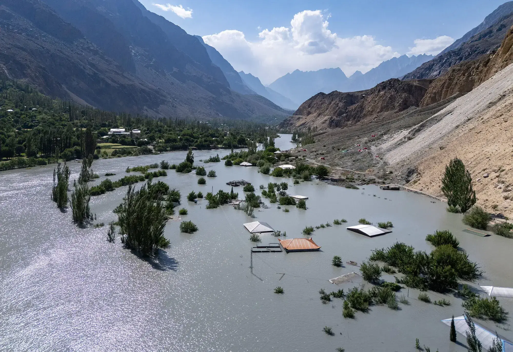An aerial view of a flooded valley in Gilgit-Baltistan, with buildings and trees standing in the water.