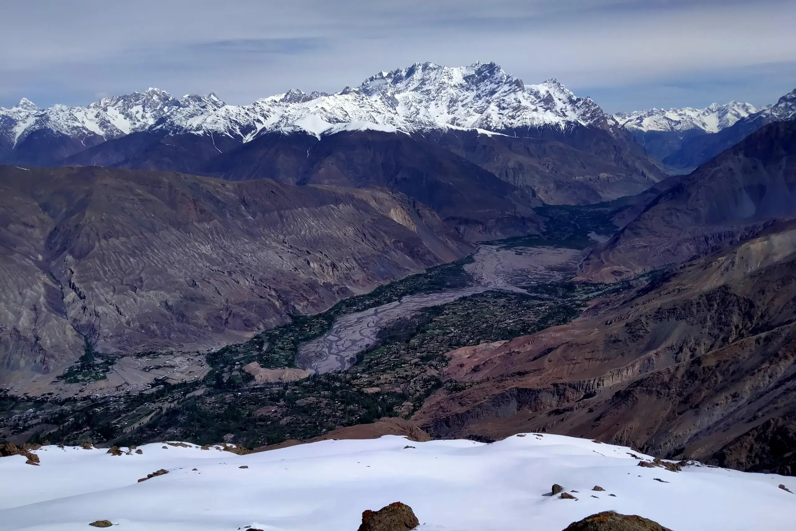 Snow in the foreground above a river valley and mountain range in northern Pakistan.